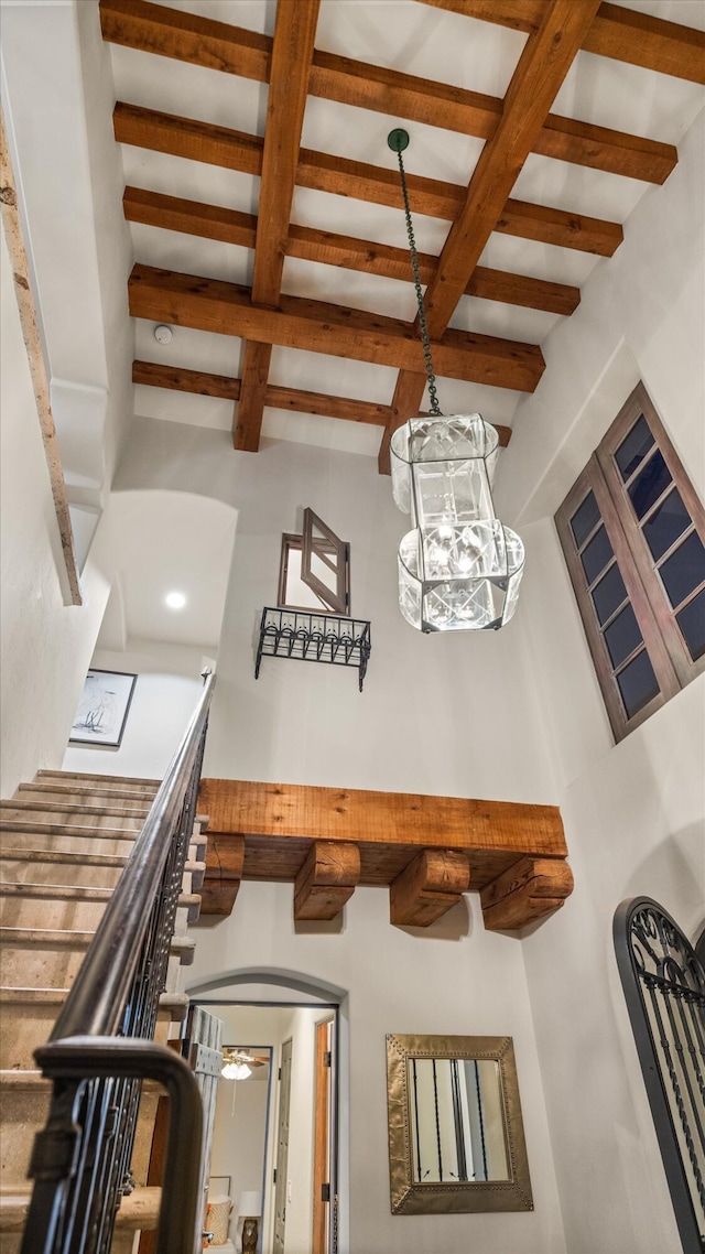 staircase with a high ceiling, arched walkways, and beamed ceiling