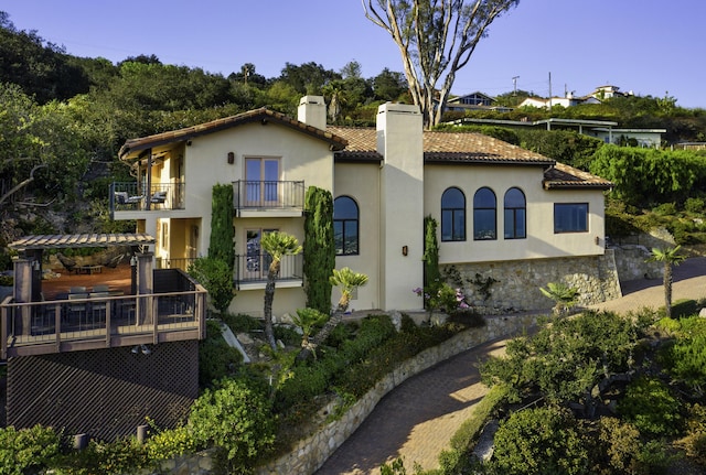 view of front facade with a tiled roof, a chimney, and stucco siding