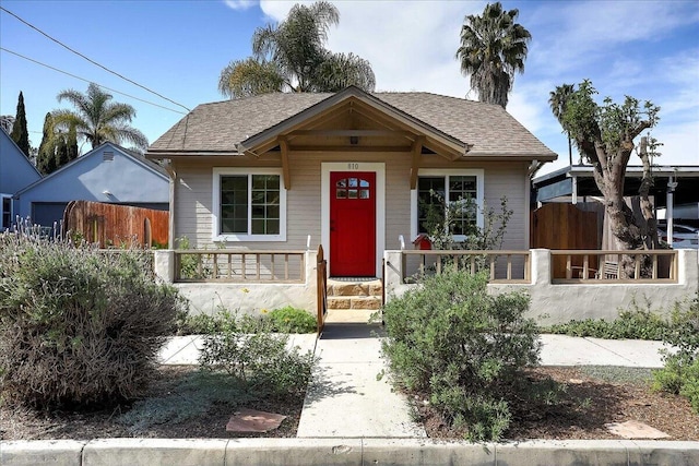 bungalow with a porch, fence, and a shingled roof