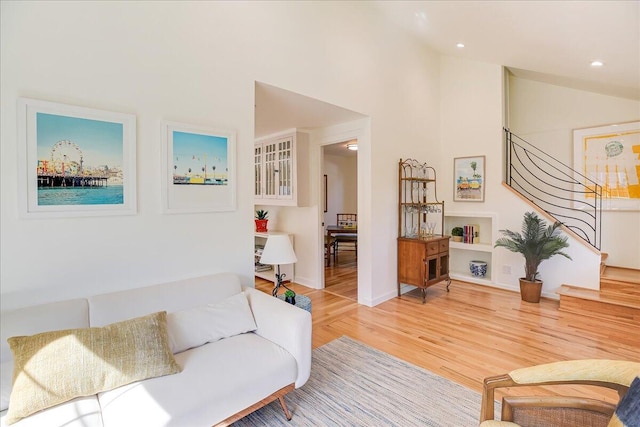 living area featuring light wood finished floors, baseboards, stairway, high vaulted ceiling, and recessed lighting