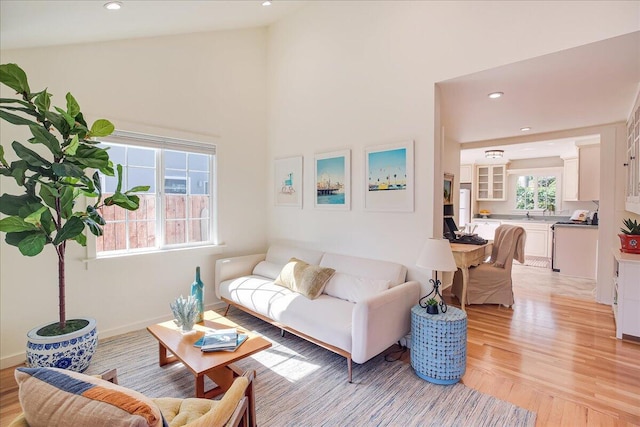 living room featuring baseboards, high vaulted ceiling, light wood-style flooring, and recessed lighting