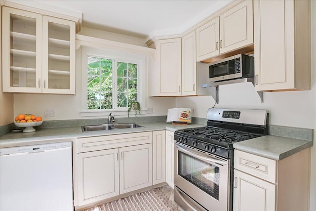 kitchen with light countertops, appliances with stainless steel finishes, a sink, and glass insert cabinets