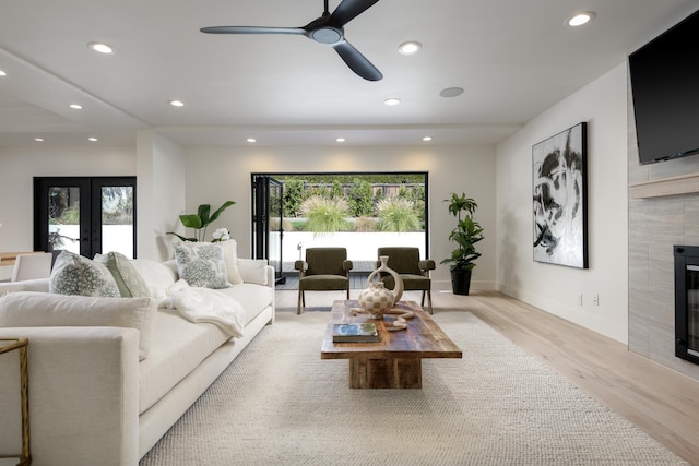 living room featuring a tiled fireplace, recessed lighting, light wood-style flooring, and french doors