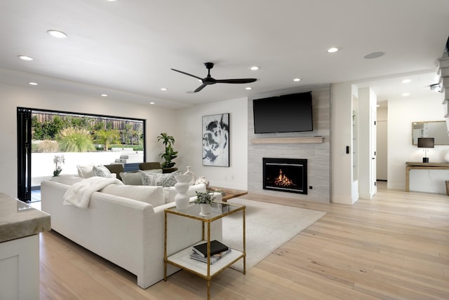 living area with recessed lighting, a large fireplace, a ceiling fan, and light wood finished floors