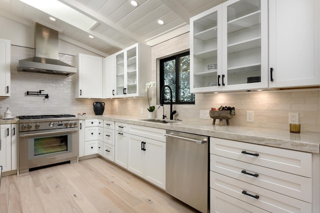 kitchen featuring vaulted ceiling with beams, light wood-style flooring, stainless steel appliances, wall chimney exhaust hood, and a sink