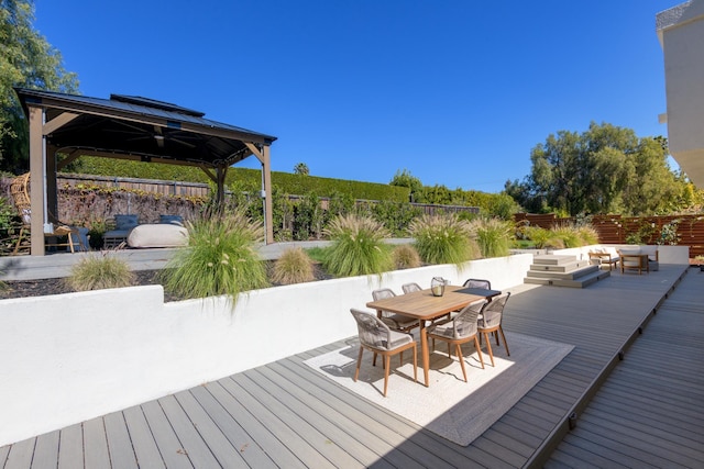 wooden terrace with a gazebo, outdoor dining area, and fence