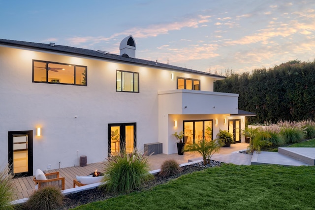 back of property at dusk featuring a lawn, a wooden deck, central AC, and stucco siding