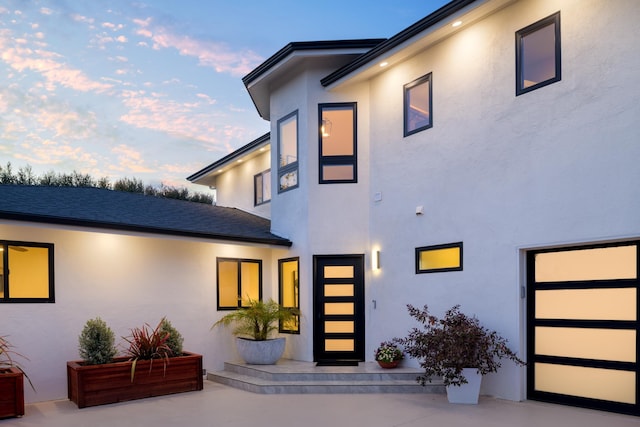 exterior space with stucco siding, a shingled roof, and a patio