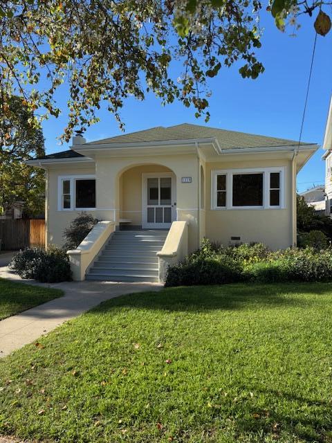 bungalow-style home featuring fence, a front lawn, and stucco siding