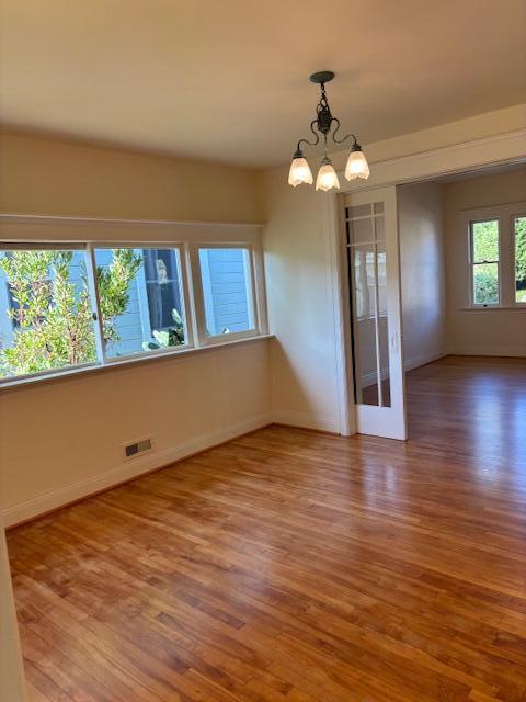 empty room featuring baseboards, a chandelier, and wood finished floors