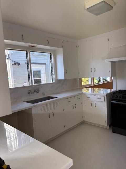 kitchen featuring light countertops, white cabinets, black range with gas cooktop, and a sink