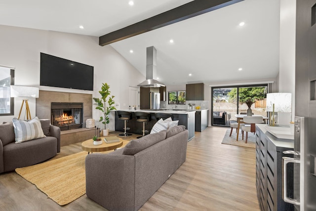 living room with high vaulted ceiling, light wood-style flooring, recessed lighting, beamed ceiling, and a tiled fireplace