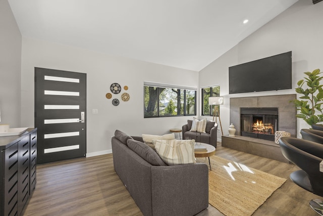 living area with high vaulted ceiling, a tile fireplace, recessed lighting, wood finished floors, and baseboards