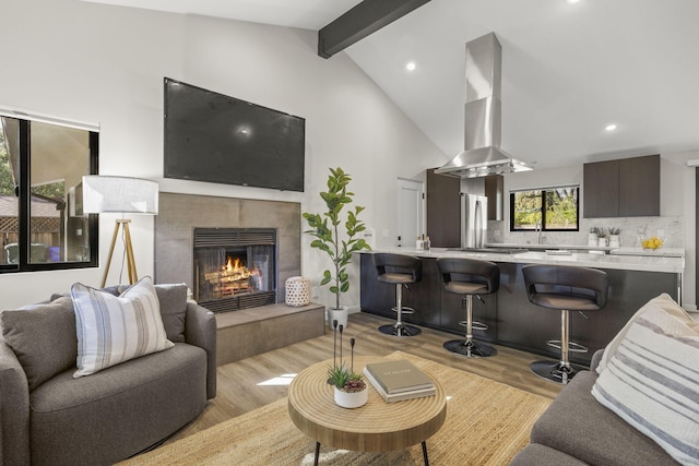 living room with recessed lighting, vaulted ceiling with beams, light wood-style flooring, and a tiled fireplace