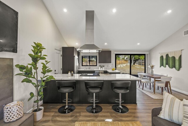 kitchen with a breakfast bar, freestanding refrigerator, a peninsula, and wall chimney exhaust hood