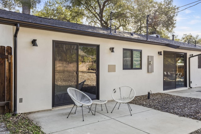 rear view of property with a shingled roof, a patio area, and stucco siding