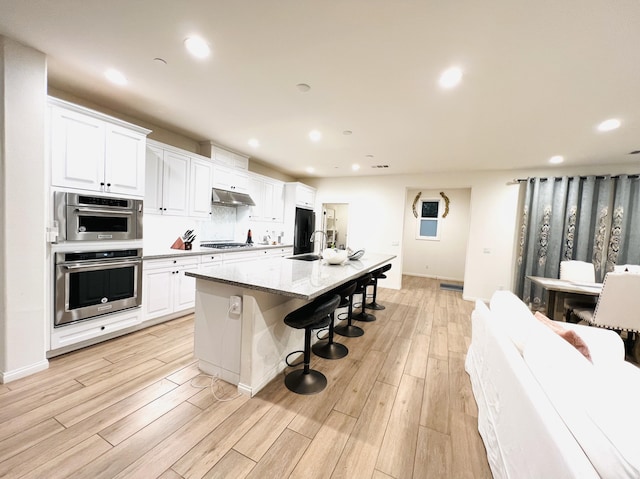 kitchen with a breakfast bar, under cabinet range hood, a sink, stainless steel appliances, and light wood-style floors