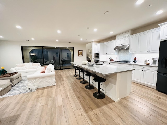 kitchen with under cabinet range hood, black fridge, stainless steel gas cooktop, and light wood-type flooring