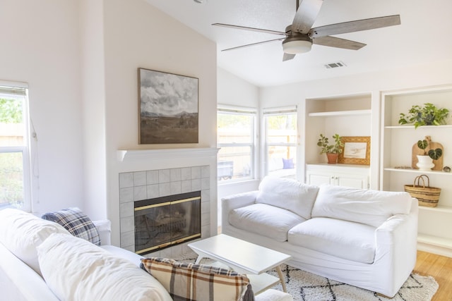 living area with visible vents, a tiled fireplace, ceiling fan, vaulted ceiling, and wood finished floors