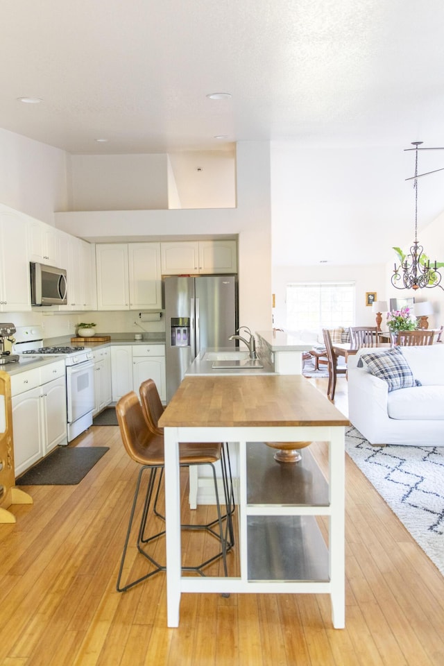 kitchen featuring stainless steel appliances, light wood-style flooring, white cabinetry, a sink, and a chandelier