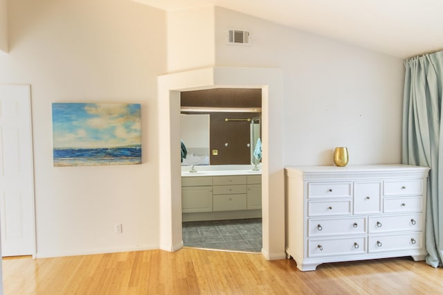 bedroom featuring light wood finished floors, lofted ceiling, visible vents, ensuite bathroom, and a sink