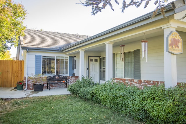 property entrance featuring a yard, brick siding, a porch, and fence