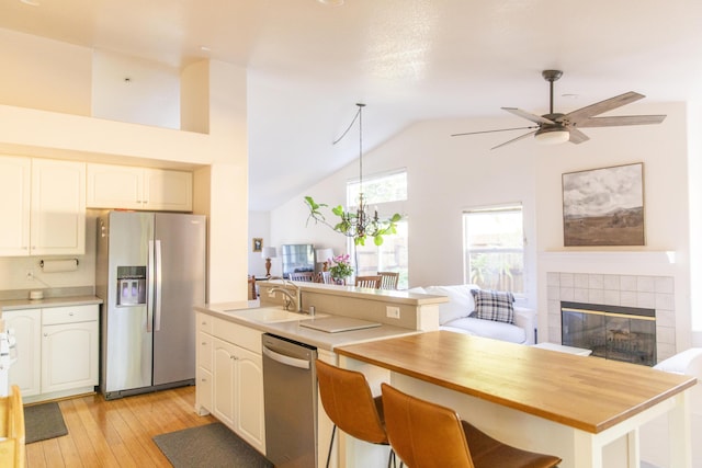 kitchen featuring light wood-style flooring, a fireplace, a sink, open floor plan, and appliances with stainless steel finishes