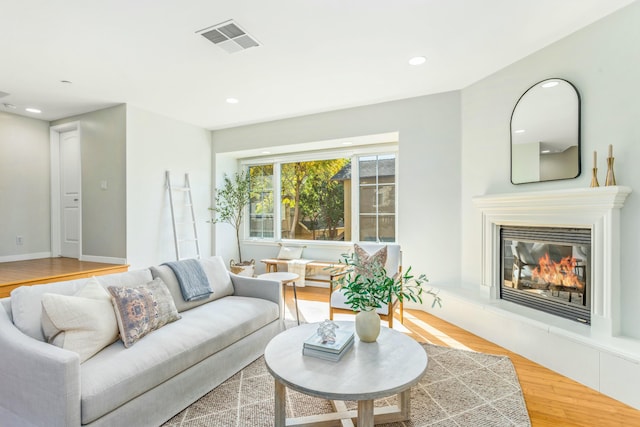 living room featuring recessed lighting, wood finished floors, visible vents, baseboards, and a glass covered fireplace