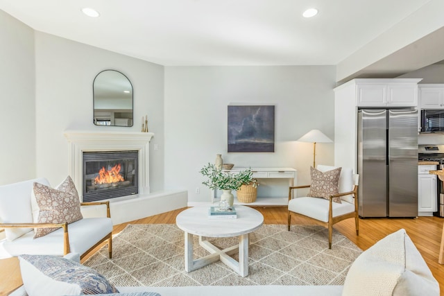 living area featuring light wood-type flooring, recessed lighting, and a glass covered fireplace