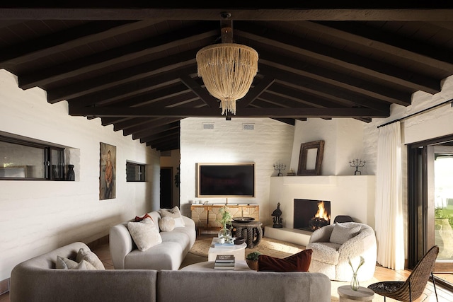 living area with lofted ceiling with beams, a lit fireplace, and a notable chandelier