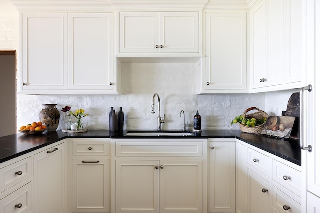 kitchen with dark countertops, tasteful backsplash, white cabinets, and a sink