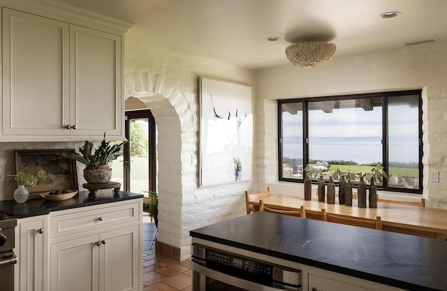 kitchen with arched walkways, brick floor, visible vents, white cabinets, and dark countertops