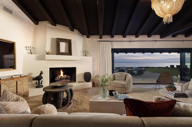 living area featuring beam ceiling, a fireplace, a notable chandelier, visible vents, and wood finished floors