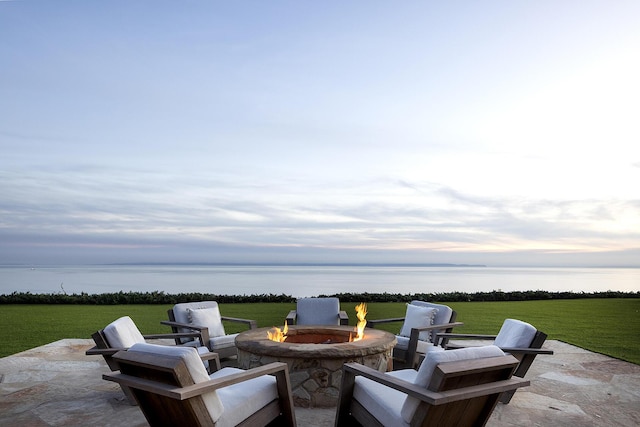 patio terrace at dusk featuring a fire pit, a yard, and a water view