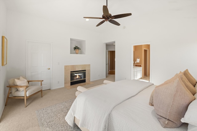 bedroom featuring a ceiling fan, a tile fireplace, light carpet, and ensuite bath