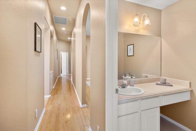 corridor featuring recessed lighting, visible vents, light wood-style flooring, a sink, and baseboards