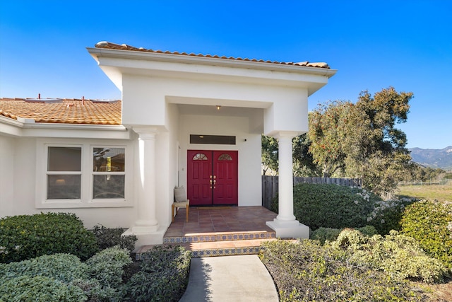 entrance to property featuring a tiled roof, fence, and stucco siding