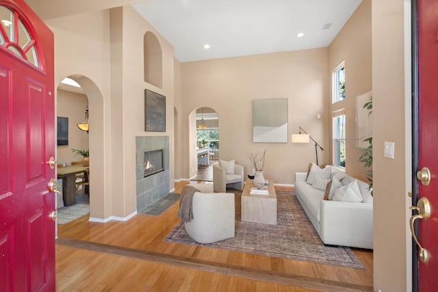 living area with arched walkways, a high ceiling, wood finished floors, baseboards, and a tiled fireplace