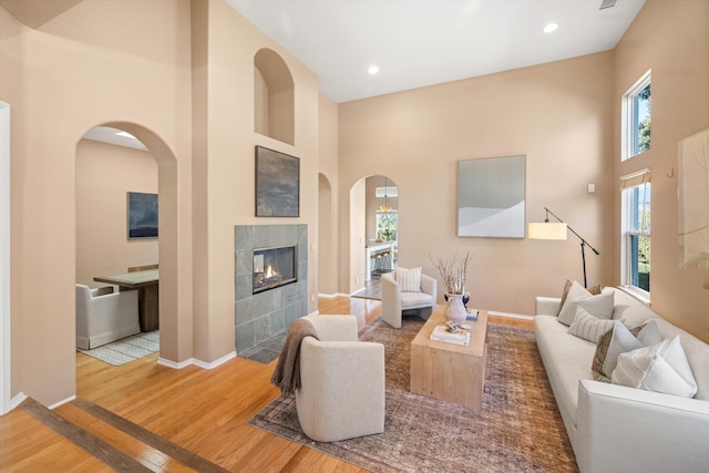 living room featuring baseboards, a tiled fireplace, a towering ceiling, wood finished floors, and recessed lighting