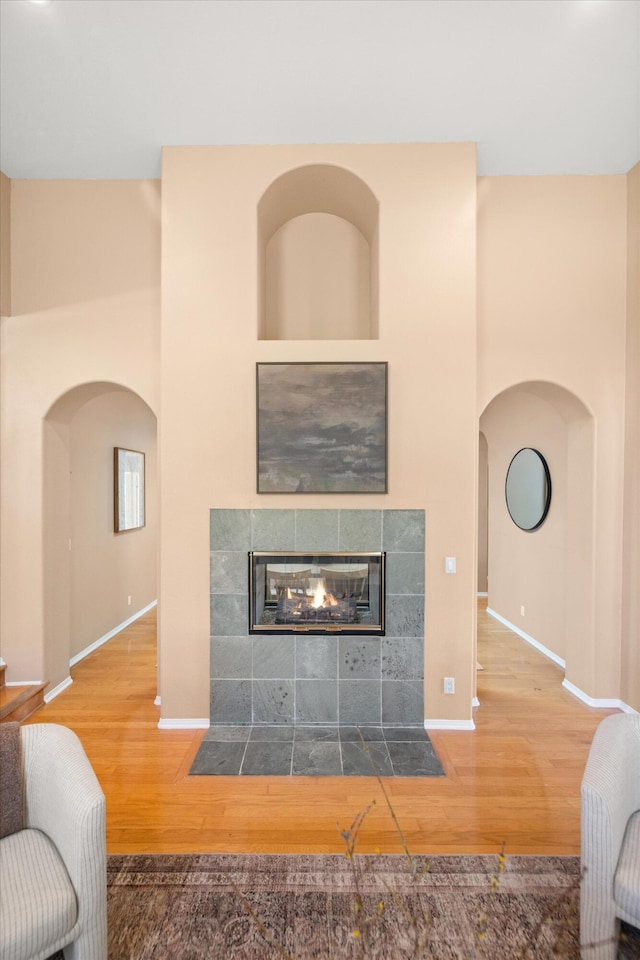 living area featuring arched walkways, a fireplace, wood finished floors, and baseboards