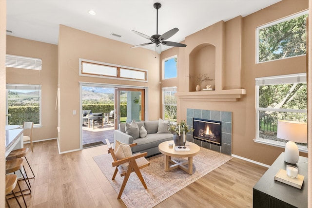 living room featuring visible vents, a high ceiling, wood finished floors, a tile fireplace, and baseboards