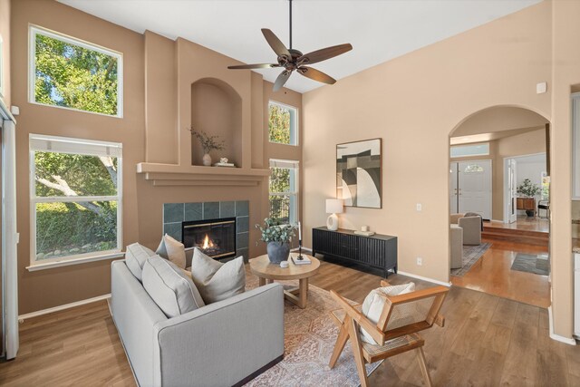 living area with a high ceiling, baseboards, a tiled fireplace, and wood finished floors