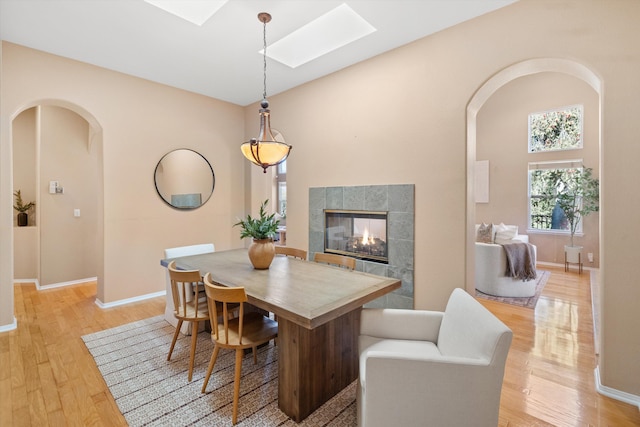 dining space with light wood-type flooring, a skylight, a fireplace, and arched walkways