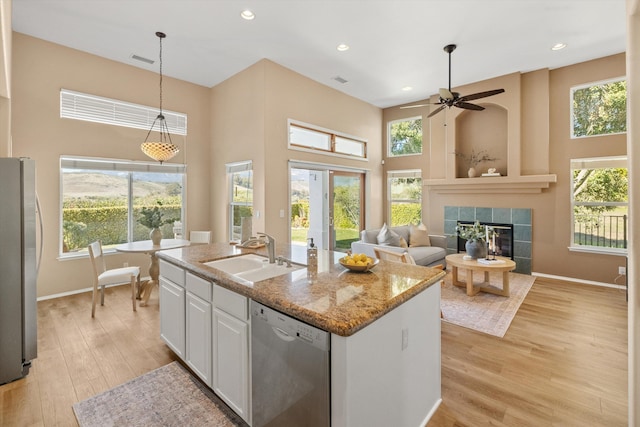 kitchen featuring white cabinets, a tiled fireplace, light wood-style flooring, stainless steel appliances, and a sink