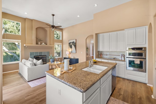 kitchen with arched walkways, stainless steel appliances, wood finished floors, a sink, and a tiled fireplace