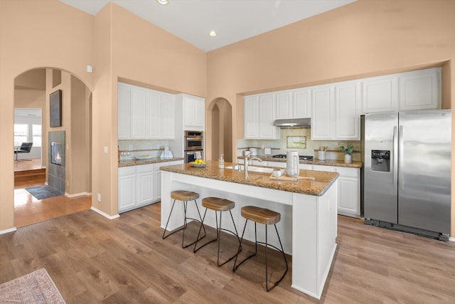 kitchen featuring light wood-type flooring, under cabinet range hood, appliances with stainless steel finishes, and arched walkways