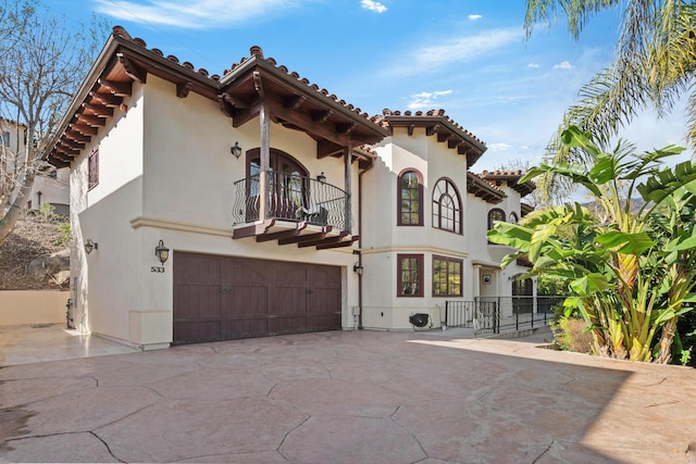 mediterranean / spanish home featuring a balcony, a garage, a tiled roof, concrete driveway, and stucco siding