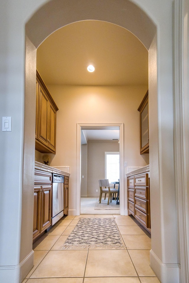 kitchen featuring light tile patterned floors, baseboards, brown cabinetry, stainless steel dishwasher, and recessed lighting