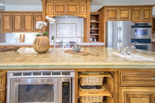 kitchen with stainless steel appliances, brown cabinetry, a sink, and tile counters