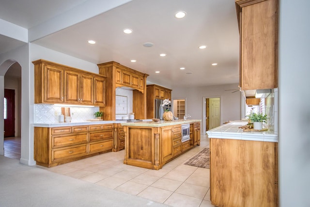 kitchen with arched walkways, stainless steel appliances, tasteful backsplash, and light tile patterned floors